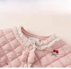 Détail de la veste en coton rose matelassé avec col en dentelle, nœud et broderie cerise