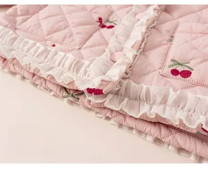 Gros plan sur la veste matelassée rose pour enfant avec broderie cerise et bord en dentelle
