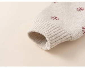 Detailed close-up of ribbed cuffs and red snowflake embroidery on beige knit sweater