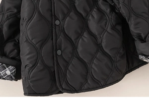 Detailed macro view of black wavy quilted jacket with snap buttons and plaid lining cuffs