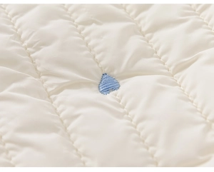 Détail du pantalon matelassé pour fille avec broderie coeur bleu sur tissu blanc cassé