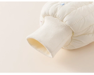 Détail macro du poignet en tricot côtelé crème et tissu matelassé avec broderies fines