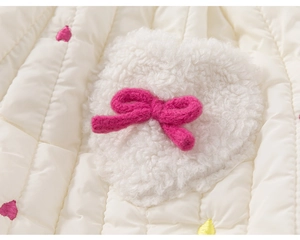 Détail du tissu en coton matelassé avec patch cœur en peluche et nœud rose tricoté