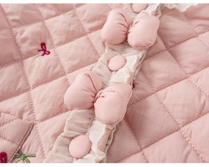 Gros plan sur tissu rose matelassé avec broderie cerise et détails de volants