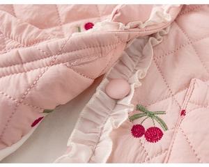 Détail d'une veste matelassée rose pour enfant avec broderie cerise et bordure dentelle