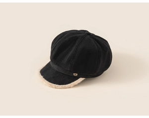 Detail of black newsboy cap with beige faux fur trim and golden metal R letter decoration