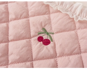 Détail du tissu matelassé rose avec broderie de cerise et bordure à volants blancs