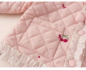 Détail du tissu matelassé rose avec broderie cerise et dentelle sur le manteau enfant