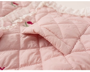 Détail du tissu matelassé rose avec broderie cerise et bordure en dentelle blanche