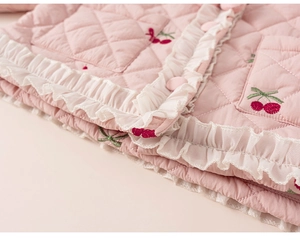 Détail d'une veste matelassée rose pour enfant avec broderie cerise et volants tulle