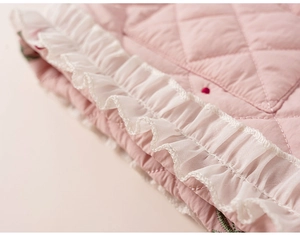 Détail de tissu rose matelassé avec broderie florale et bordure en dentelle plissée