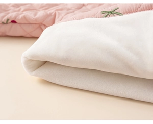 Détail du tissu matelassé rose avec broderie cerise et doublure en polaire blanche