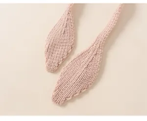 Detail of light pink knit hat featuring leaf-shaped strap ends and fine woven texture