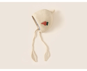 Close-up of cream knit baby earflap hat with decorative carrot patch and tie straps