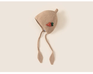 Detail of beige knit baby earflap hat featuring a cute 3D carrot accent and leaf-shaped ties