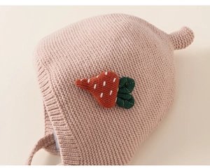 Detail of pink knitted baby hat featuring a 3D strawberry patch and soft chin straps