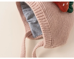Detailed macro view of pink knit baby hat with red strawberry and soft grey cotton lining