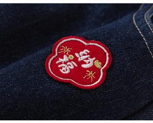 Detail of red plum blossom embroidery with festive Chinese characters on blue denim