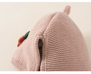 Detail of pink knit baby hat featuring coarse wool texture and carrot fabric ornament
