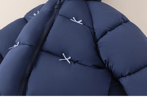 Macro detail of navy quilted kid's jacket featuring light blue bow accents and zipper