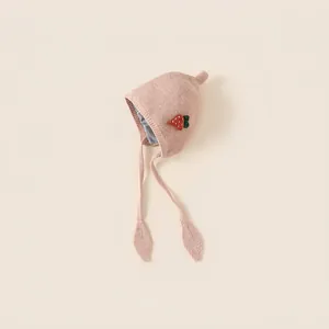 Pink knitted baby hat with strawberry decoration and earflap straps for toddlers