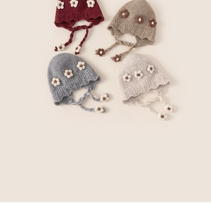 Flat lay of four knit winter hats with floral accents and braided earflaps for girls