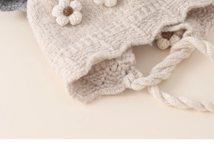 Detailed macro view of cream knitted baby hat featuring 3D crochet flowers and braided ties