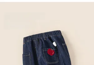 Detail view of dark blue denim jeans with elastic waistband and apple embroidery patch