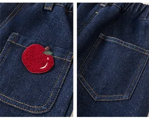 Detail of kids winter denim jeans with apple embroidery and yellow stitching