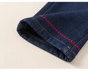 Detail of dark blue denim jeans with red polka dot embroidery and ginger yellow stitching