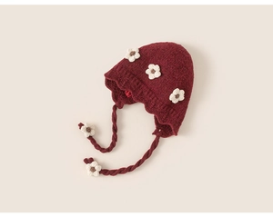 Detail of dark red knit winter hat with 3D white flower crochet and earflaps