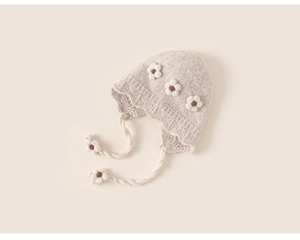 Detail of hand-knitted baby earflap hat with 3D floral accents and warm beige texture