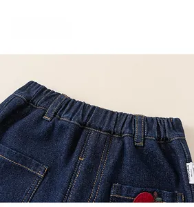 Detail of kids denim pants showing elastic waist with contrast orange stitching and embroidery