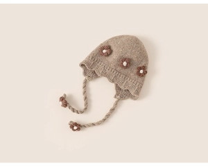 Detailed close-up of beige knitted baby earflap hat with brown floral accents and ties