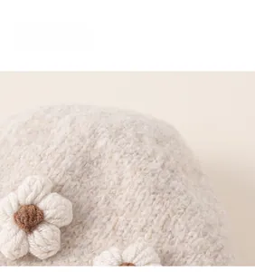 Close-up of beige knit winter hat featuring white crochet flowers and soft wool texture