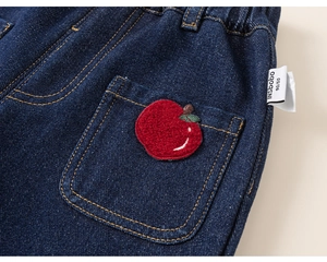 Detail of red apple embroidery on dark blue fleece-lined denim pants for kids