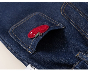 Detail of dark blue denim pants with a red apple embroidery and gold contrast stitching