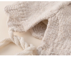 Close-up of beige thick knit baby winter hat with wave lace edge and woven ties