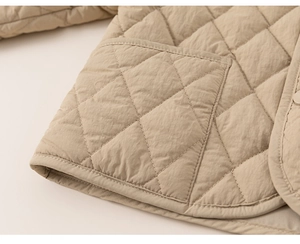 Close-up of quilted diamond pattern and large patch pocket on kids light beige jacket