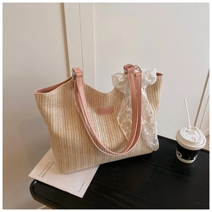 Detailed close-up of a beige woven straw tote bag with pink straps and a lace scarf detail