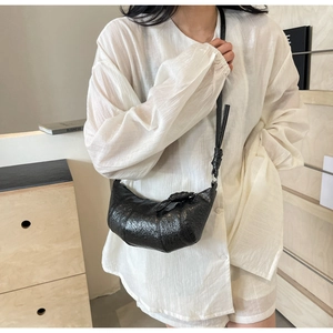 Détail du sac croissant noir avec bandoulière nouée et texture cuir porté par un mannequin