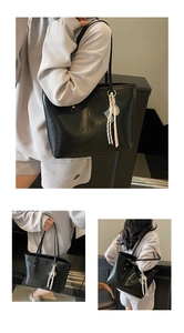 Detail view of large black tote bag featuring glossy faux leather and braided rope charm