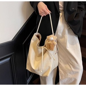 Detail of soft cream tote bag with stylish drawstring closure and cute plush bear charm
