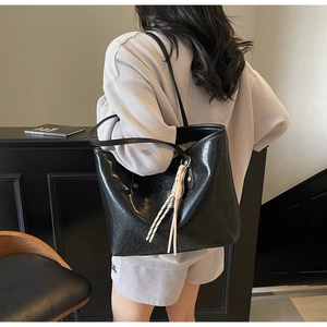 Detailed view of black large-capacity tote bag with woven pendant on model shoulder