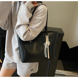 Close-up of a black leather tote bag with lychee texture and creative tennis racket charm