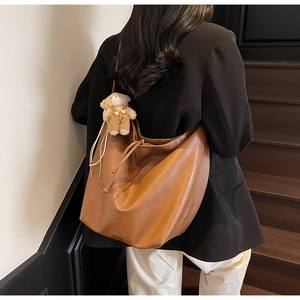 Brown soft leather tote bag with plush bear charm worn by model on stairs