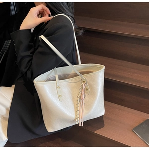 Detail of minimalist beige tote bag with soft glossy texture and woven tassel charm