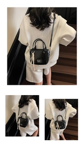 Detailansicht der schwarzen Eimertasche mit weißem Logo und Quasten-Anhänger