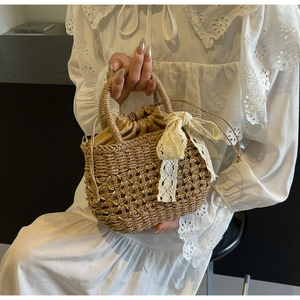 Détail du sac en paille tressée avec nœud en dentelle blanche et fils dorés fins