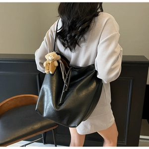 Detail of black leather tote bag with soft matte finish and cute teddy bear keychain charm